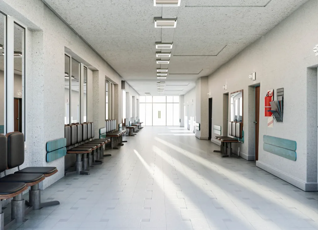 Illustrative image: An empty hospital corridor with doors and seating along its sides.