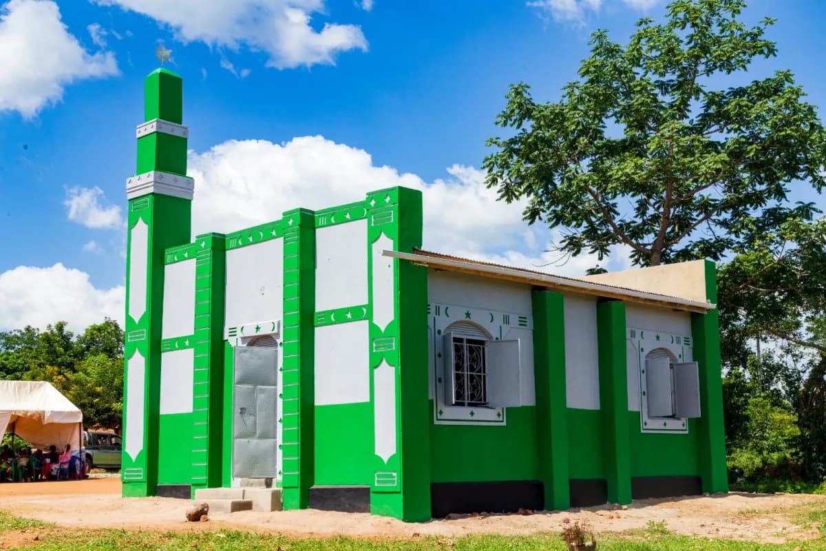 A green and white masjid with a minaret under a blue sky