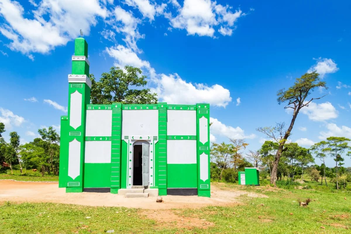 A small green and white masjid across an open yard