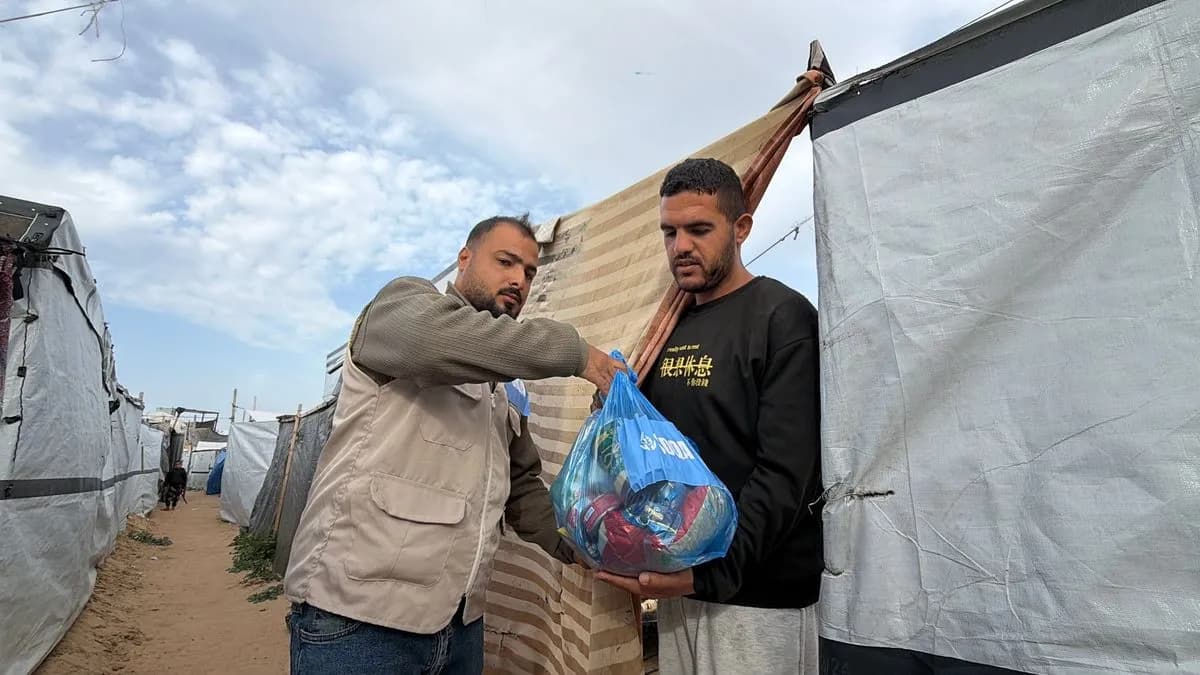 An SDQA volunteer handing a food pack to a man among the tents in Gaza